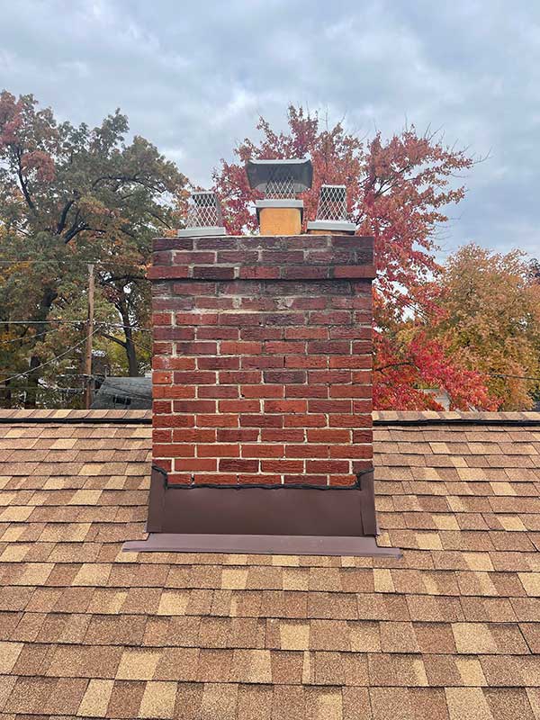 Stock photo of chimney crown - Before rebuild with black spalling, caps and flues crooked and falling off the top. Fall trees in the background.