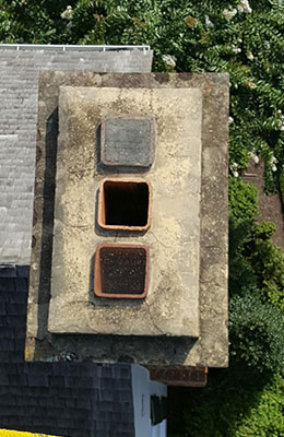 Stock photo of triple chimney flue and crown before repairs.  The photo is looking down into the flues.  There is a roof and trees in the background.