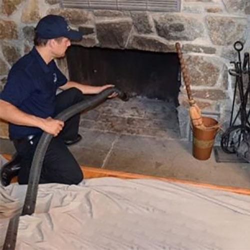 Stock photo of tech vacuuming out fireplace.  The Fireplace is built of stone.  There is a tarp on the floor