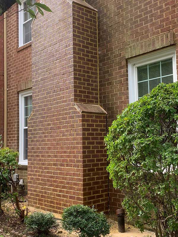 Nice large brick chimney on side of large house.  Pretty landscaping and 3 windows.