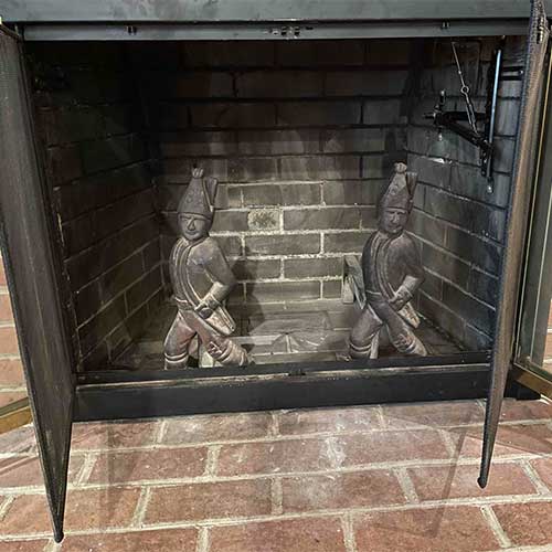 Stock photo of English warrior fire dogs inside fireplace with brick surround and open doors on the front.
