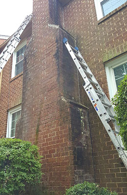 Large home and chimney with soot all over the outside of chimney.  Ladders placed on each side for cleaning.