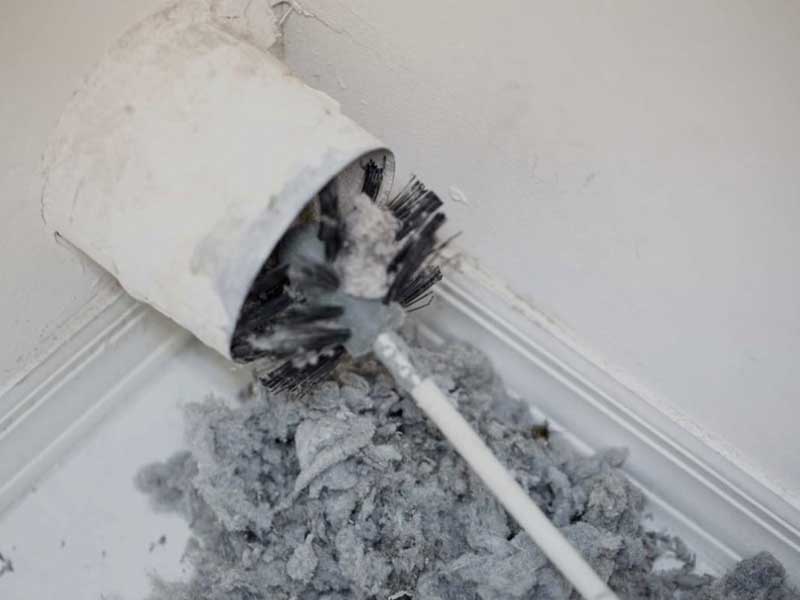 Stock photo of cleaning dryer vent with a wire brush.  Lint all over the floor and brush.