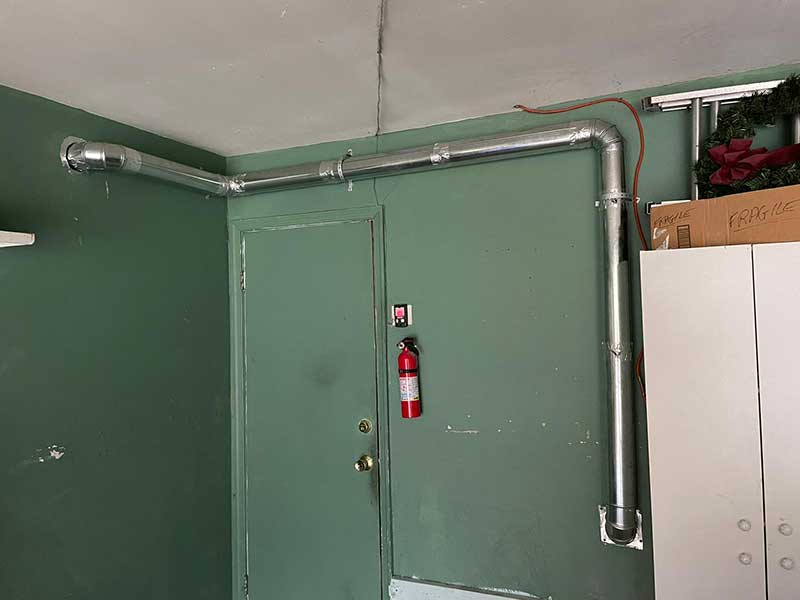 Stock photo of dryer vent line after installation in basement with fire extinguisher to the right of the access door.