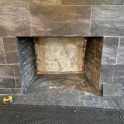 Stock photo of firebox before rebuild.  No firebrick on the back wall of the firebox.  Limestone tile surround.