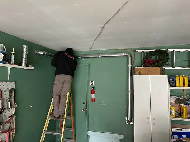 Stock photo of tech on ladder installing dryer vent line in basement.